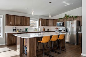 Eine moderne Küche mit Holzschränken, einem Edelstahlkühlschrank, einer Mikrowelle und einer großen Kochinsel mit Barhocker.