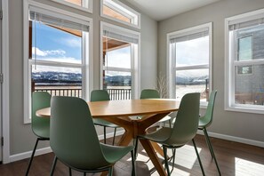 Ein Essbereich mit einem runden Tisch und sechs Stühlen, großen Fenstern mit Blick auf eine verschneite Landschaft und einem Balkon mit Geländer.