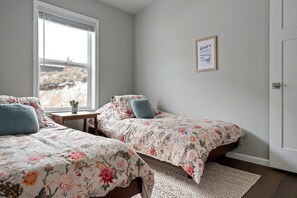 Ein Schlafzimmer mit zwei Einzelbetten, einem kleinen Tisch, einer Topfpflanze und einem gerahmten Zitat an der Wand.