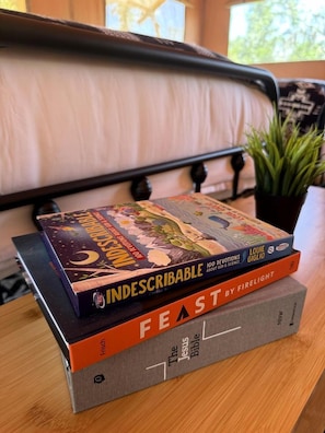 A stack of books on a wooden table with a plant in the background.