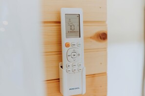 A white thermostat with a digital display, buttons for mode, set, OK, and other functions, and the brand name 'MRCOOL' on the bottom.