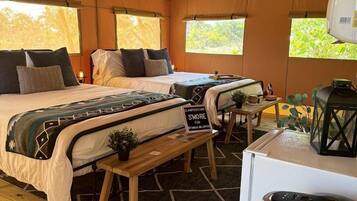 A tented accommodation with two beds, a small table, a fan, a refrigerator, and a sign indicating a fun activity.