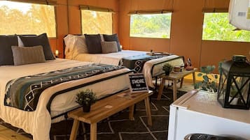 A tented accommodation with two beds, a small table, a fan, a refrigerator, and a sign indicating a fun activity.