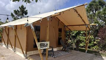 A tent with a wooden deck, a welcome sign, and a chair.