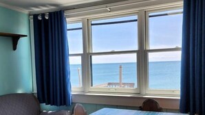 Une chambre avec un lit, une table et des chaises, une fenêtre avec des rideaux et une vue sur la mer.
