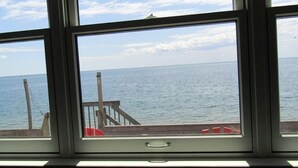 Une vue à travers une fenêtre donnant sur une terrasse en bois avec une balustrade, et offrant un panorama sur une mer calme.