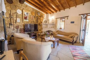 Ein rustikales Wohnzimmer mit Steinwänden, Holzbalken, einem Fernseher, Sofas und einem Kamin.