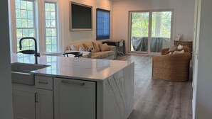 A modern kitchen with a marble island, white cabinetry, and a dining area with a sofa and wicker chairs. - 3-bedroom marsh views in Litchfield by the Sea with many amenities (Pawleys Island)