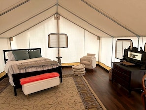A tent-style bedroom with a bed, bench, chair, and dresser.