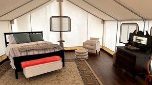 A tented room with a bed, a chair, a desk, and a lamp.