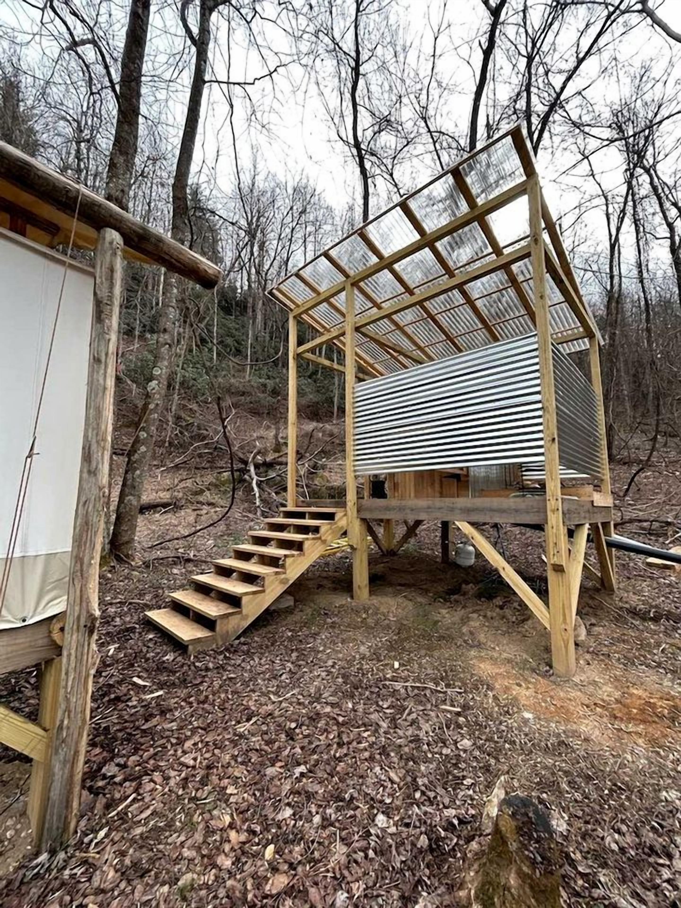 Eine Holzhütte mit einem Metall-Dach, einer Treppe und einem kleinen, abgeschlossenen Bereich.