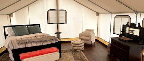 A tent-style bedroom with a bed, bench, chair, and dresser.