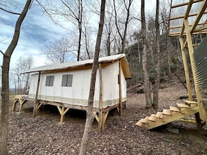 A wooden cabin with a ramp leading to a staircase, surrounded by trees.