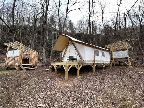 Three wooden cabins with elevated platforms, a table, and chairs in a forested area.