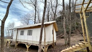 A wooden cabin with a ramp leading to a staircase, surrounded by trees.