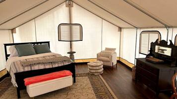 Een slaapkamer in tentstijl met een bed, een bankje, een stoel en een dressoir.