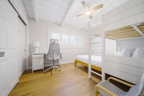 Ein Zimmer mit Etagenbett, Schreibtisch, Stuhl und Deckenventilator.