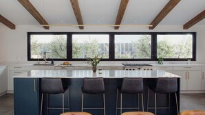 Een moderne keuken met een centraal eiland, barstoelen en grote ramen.