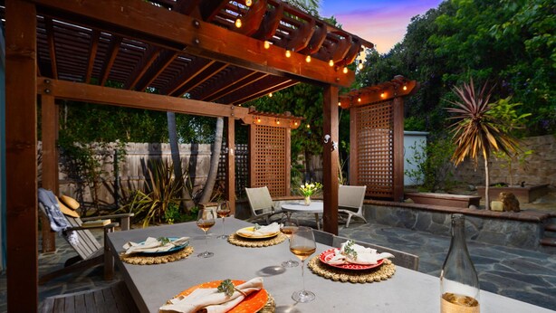 Een buiten eethoek met een pergola, tafels gedekt met borden, glazen en een fles.