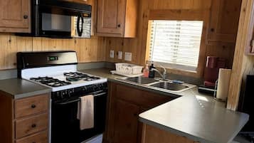 A compact RV kitchen with a stove, microwave, and sink.