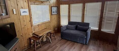 A wooden cabin interior with a ceiling fan, a sofa, a table, and a TV.