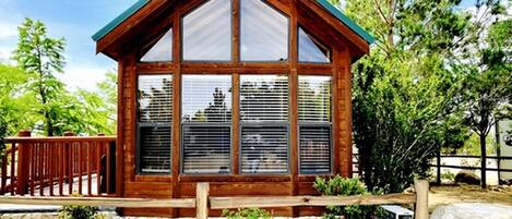 A wooden cabin with a pitched roof, large windows, and a stone foundation.