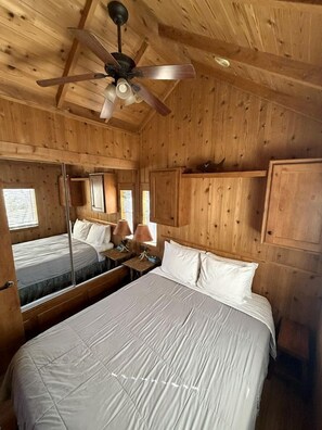 Een houten kamer met een bed, een plafondventilator, een spiegel en een raam.