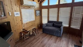 A wooden cabin interior with a ceiling fan, a sofa, a table, and a TV.