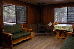 Interior acogedor de una cabaña con detalles de madera, un sofá verde, una mesa de comedor con mantel estampado de limones y un estufa de leña.