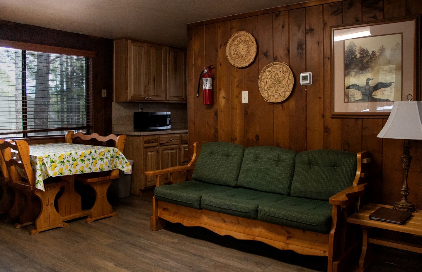 Una habitación acogedora con un sofá de madera, una mesa de comedor con sillas, una zona de cocina y un cuadro en la pared.