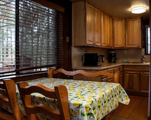 Una cocina con armarios de madera, una mesa de comedor con mantel estampado de limón y una ventana con persianas.
