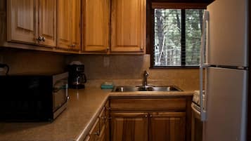 A kitchen with wooden cabinets, a stainless steel sink, a microwave, and a refrigerator.