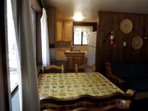 Eine kleine Küche mit Holzausstattung, einem Kühlschrank, einer Spüle und einem Esstisch mit einer blumigen Tischdecke.