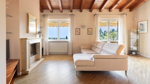 A living room with a fireplace, a sofa, and a view through large windows. - Marietta Home With Lake View by Wonderful Italy (Gardone Riviera)