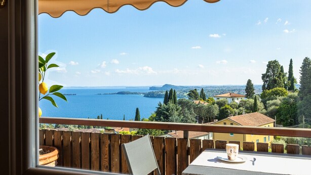 A balcony with a view of a lake and distant hills, wooden fence, and a table with a cup. - Marietta Home With Lake View by Wonderful Italy (Gardone Riviera)
