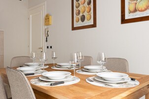 Una mesa de comedor dispuesta con platos, copas de vino y cubiertos, rodeada de sillas.