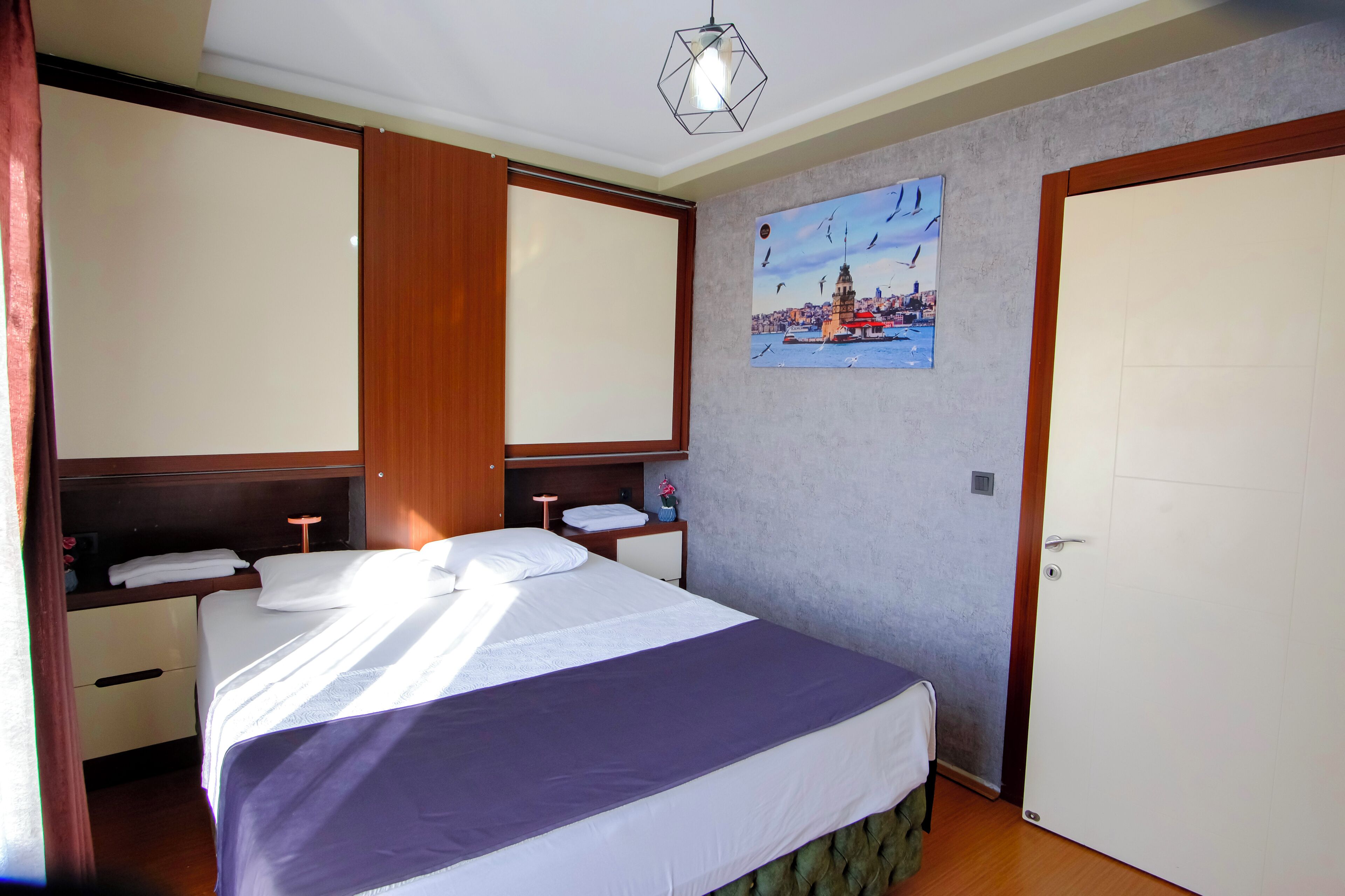 Un dormitorio con una cama, una mesita de noche, un estante en la pared, una puerta y un cuadro.