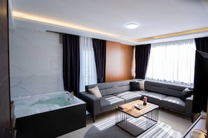 Uma sala de estar moderna com um sofá seccional, uma parede de destaque em madeira, uma janela grande com cortinas, uma banheira de hidromassagem integrada e uma mesa de centro.