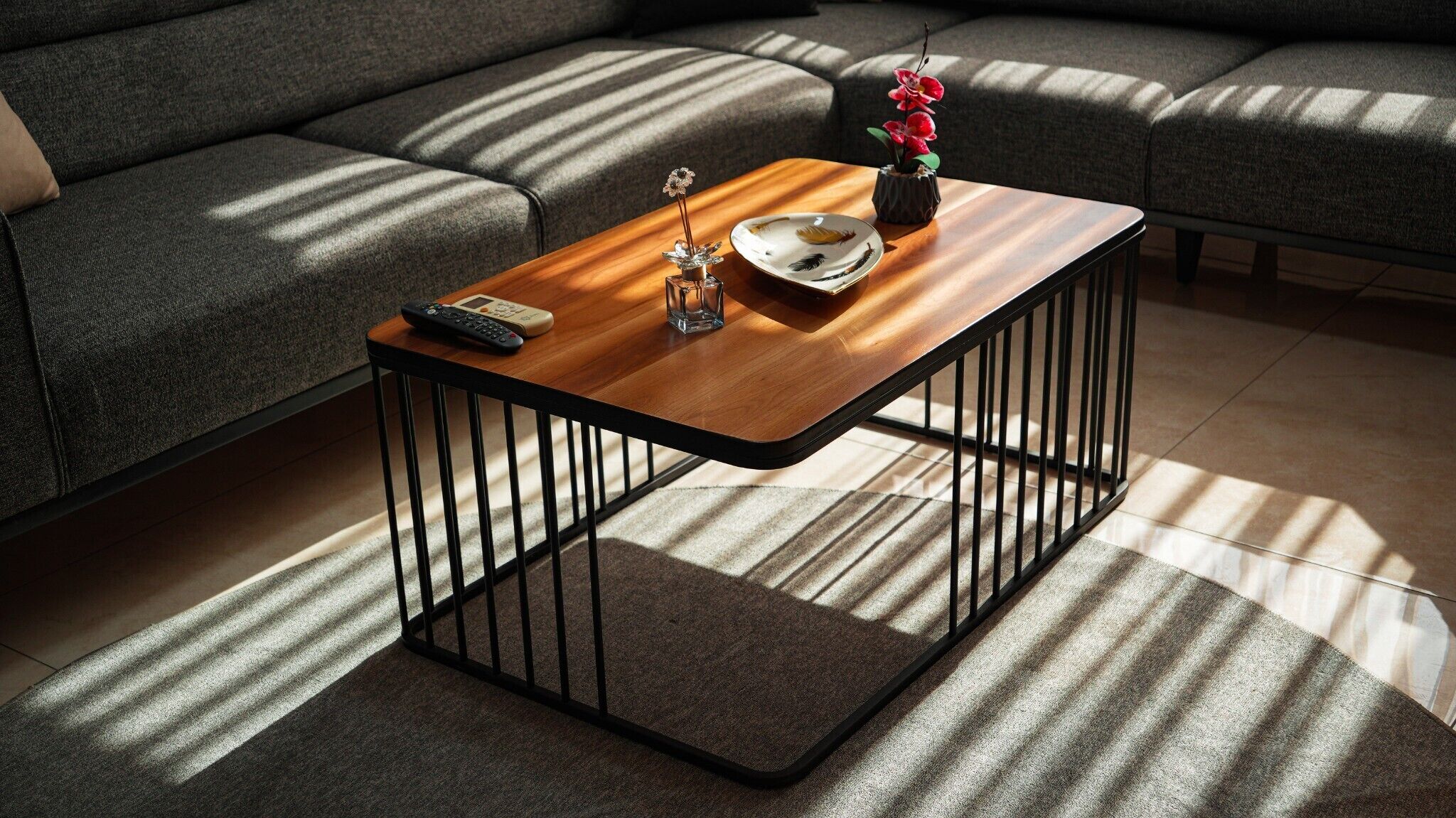 A modern living room with a sectional sofa, a wooden coffee table with a remote control, decorative items, and a patterned rug.