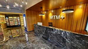 Un área de recepción con mostrador de mármol, paneles de madera y un letrero que dice 'MTM+'.