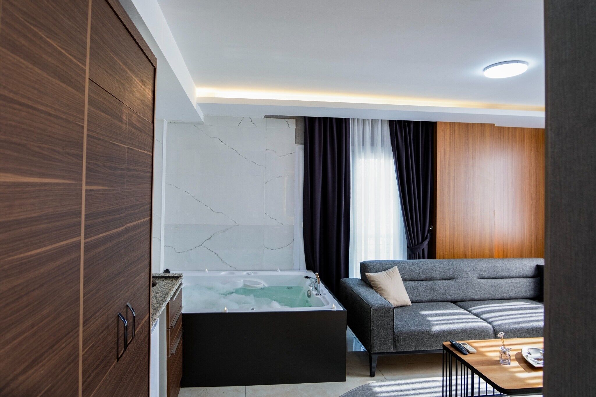 A modern room with a spa tub, a grey sofa, and a wooden cabinet.