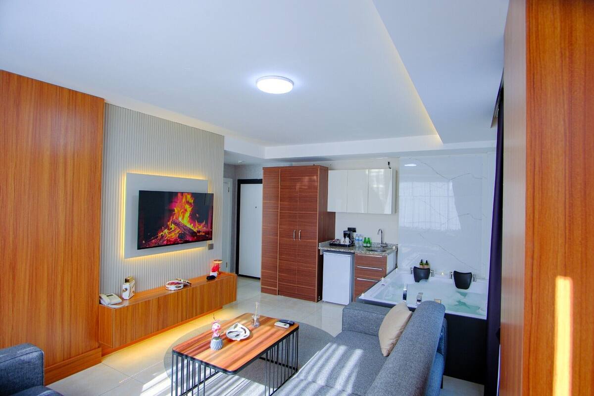 A modern living room with a TV, sofa, coffee table, and a small kitchen area.