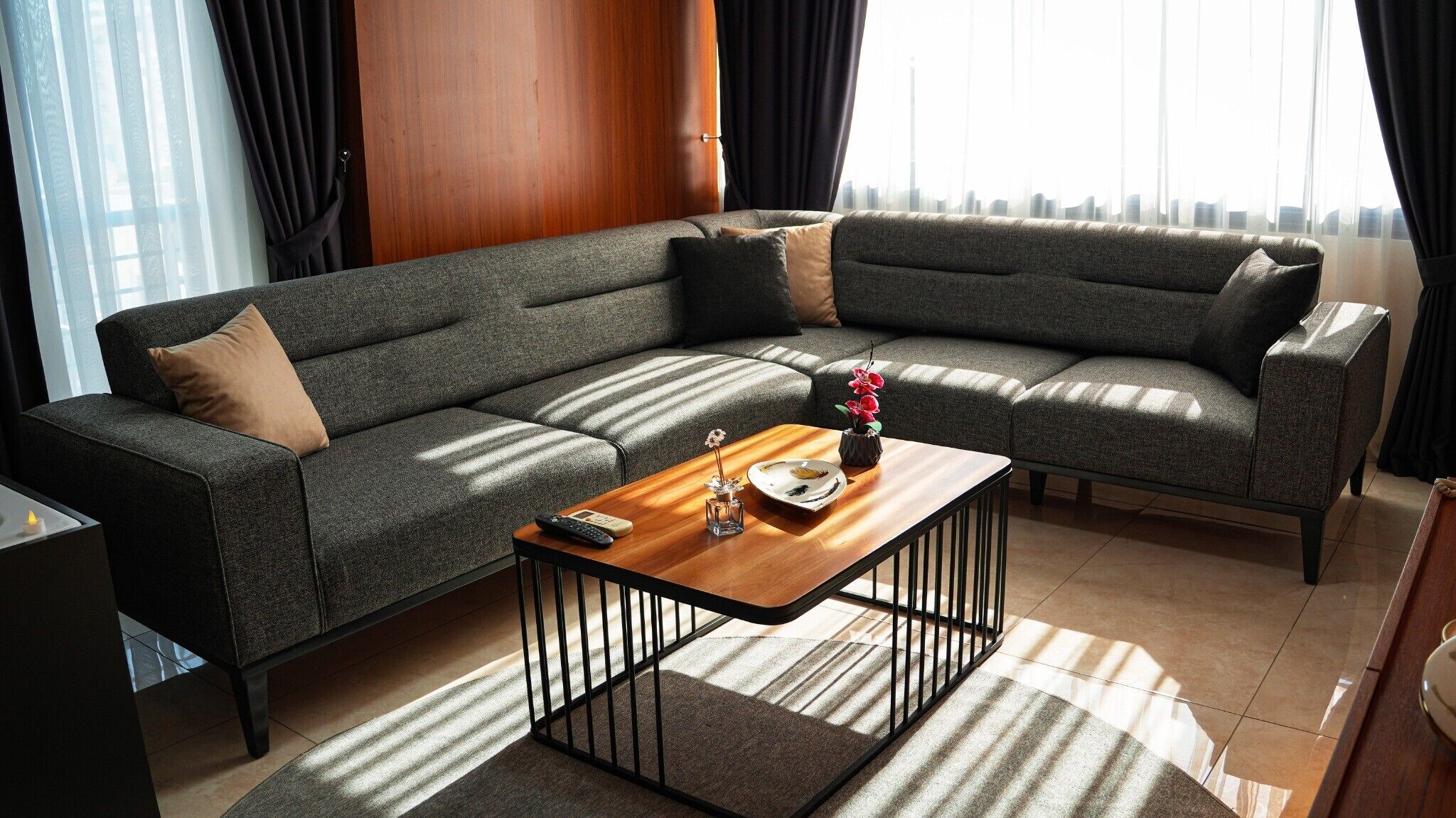A modern living room with a sectional sofa, a wooden coffee table, and a view of a cityscape through large windows.