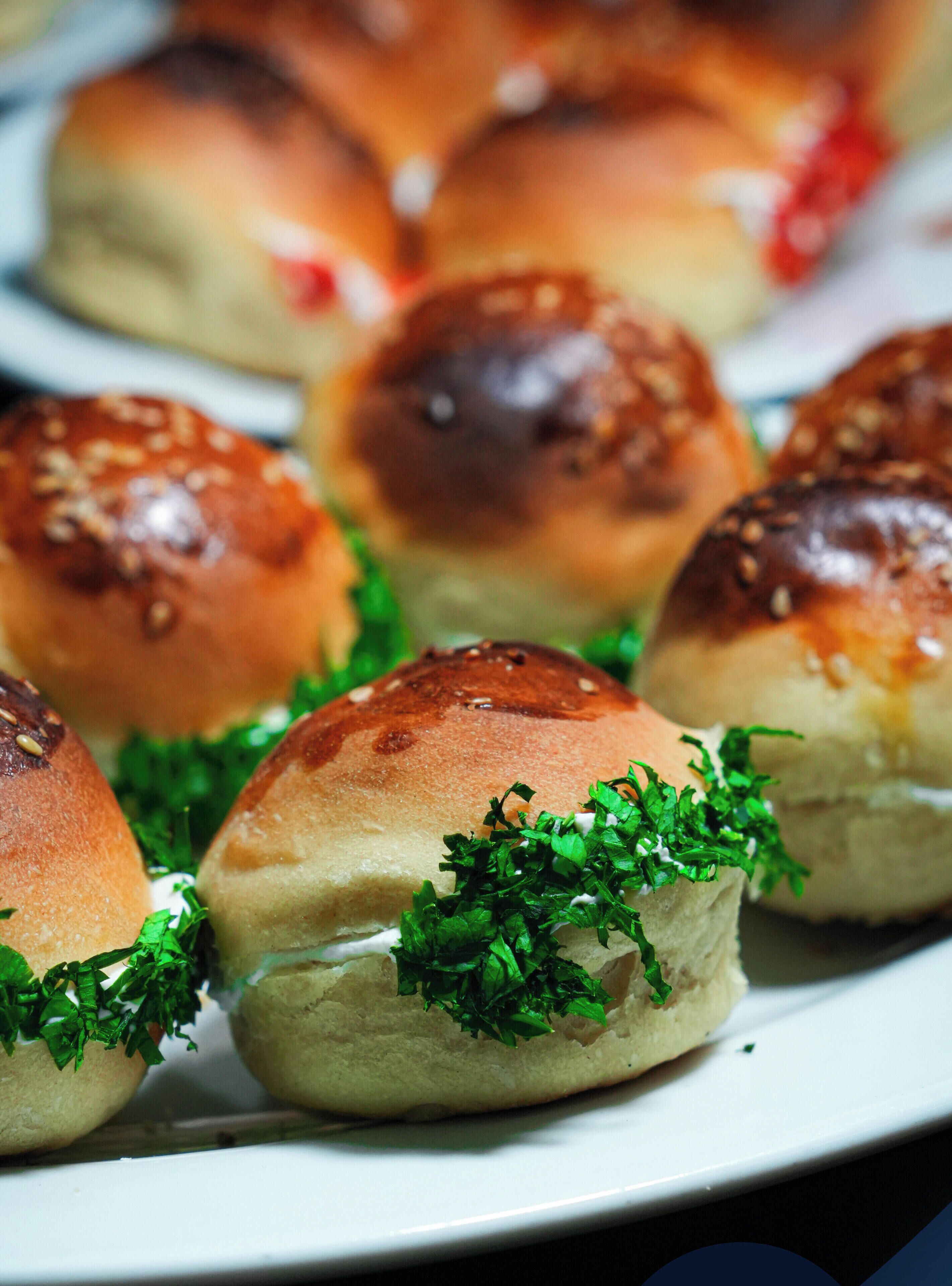 A plate of bread rolls with sesame seeds and parsley garnish.