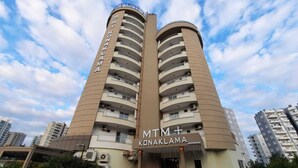 Un hotel de varios pisos con balcones, una entrada principal y un cielo despejado.