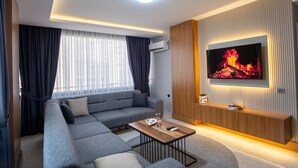 Una sala de estar moderna con sofá, una mesa de centro, un televisor montado en la pared y una ventana con cortinas.