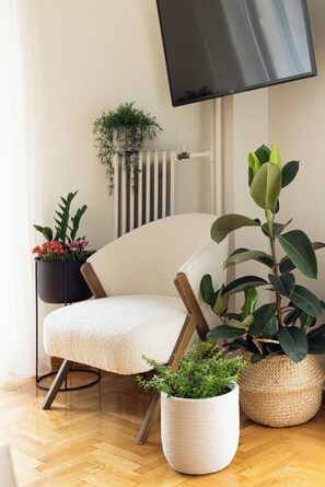 A modern living room with a comfortable armchair, a flat-screen TV mounted on the wall, and several potted plants. - Family Apartment | 50m from Acropolis Museum | 2BR 2BA (Athina)