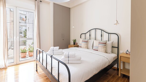 A bedroom with a bed, bedside tables, a hanging light, and a view through a window. - Family Apartment | 50m from Acropolis Museum | 2BR 2BA (Athina)