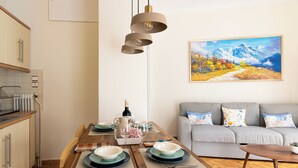 A modern kitchen with a dining area, a grey sofa, and a painting on the wall. - Family Apartment | 50m from Acropolis Museum | 2BR 2BA (Athina)