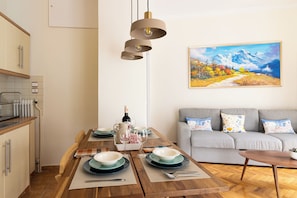 A modern kitchen with a dining area, a grey sofa, and a painting on the wall. - Family Apartment | 50m from Acropolis Museum | 2BR 2BA (Athina)